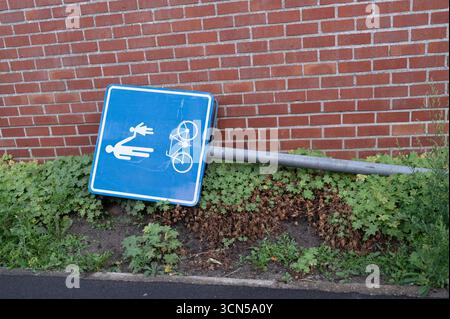 Un panneau bleu tombé, qui indique les pistes piétonnes et cyclables, est appuyé contre un mur de briques à proximité Banque D'Images