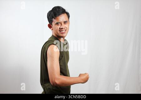 Jeune homme confiant fléchissant les biceps avec le sourire, mettant en valeur la forme physique et la santé pour le contenu de style de vie Banque D'Images
