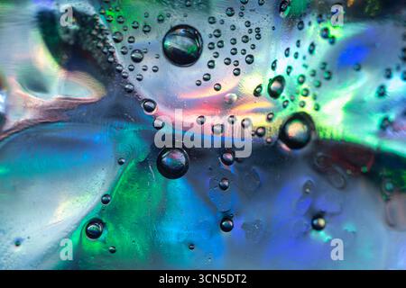 Macro photo abstraite de bulles liquides sur une surface lisse avec des couleurs vives de vert, bleu, violet et rose se mélangeant ensemble, créant R chatoyant Banque D'Images