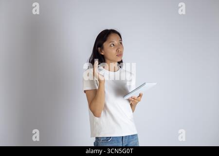 La femme tient une tablette, regarde réfléchie vers le haut, et a une main levée Banque D'Images
