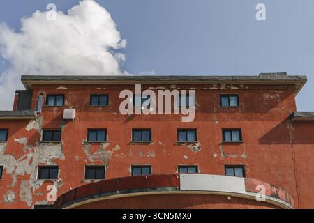 Vue d'un bâtiment orange altéré avec des fenêtres sombres se dresse sous un ciel bleu vif parsemé de nuages blancs moelleux, Isola del Gran Sasso D'italia, Abruzzes, Italie. Banque D'Images