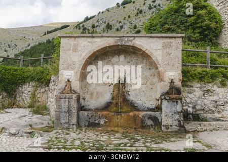 Vue d'une fontaine en pierre altérée ornée de sculptures de tête de lion, nichée sur un fond de collines ondoyantes et de verdure luxuriante, Frattura Vecchia, A Banque D'Images