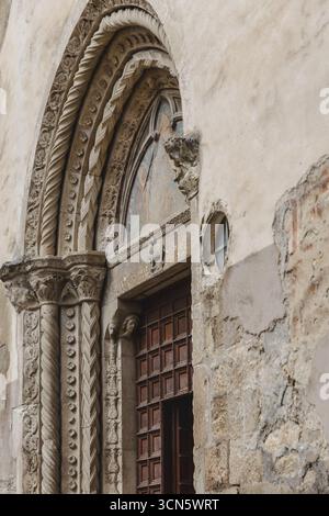 Vue de la porte détaillée et ornée d'un ancien bâtiment en pierre avec des murs altérés et une petite fenêtre ronde, Anversa degli Abruzzi, Abruzzes, Italie. Banque D'Images