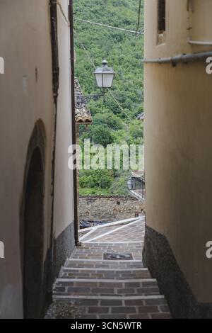 Vue d'un étroit passage avec des marches de pierre descendant entre des bâtiments anciens, révélant une colline verdoyante et une lanterne suspendue, Anversa degli Abruzzi, Banque D'Images