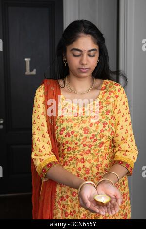 Femme indienne portant des bijoux en or debout par la porte l dans le couloir tenant la lampe à huile d'argile Banque D'Images