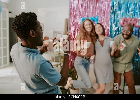 Jeune homme noir photographiant des amis multiethniques célébrant à la fête Banque D'Images