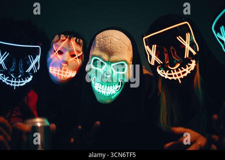 Un groupe d'individus portant des masques LED vibrants pose ensemble dans une atmosphère faiblement éclairée, évoquant une nuit animée et mystérieuse. Banque D'Images