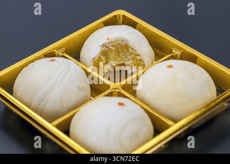 Un gâteau de lune chinois rempli de pâte de haricots, l'un avec une bouchée prise, affiché sur un plateau doré, mettant en valeur un dessert traditionnel à la texture douce et sucré Banque D'Images