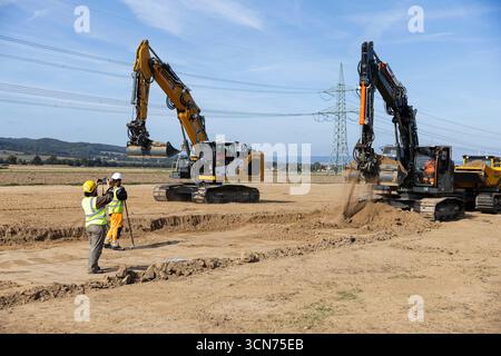 Einbeck, Allemagne. 19 septembre 2025. Les archéologues se tiennent sur un site de construction de TransnetBW près de Strodthagen dans le district de Northeim au début de la construction du « SuedLink » dans le sud de la basse-Saxe et observent comment une excavatrice enlève des couches de sol lors d'une enquête archéologique préliminaire du sol. Dans les mois à venir, les câbles de courant continu seront posés sur environ 100 kilomètres entre Elze et Friedland. La construction de SuedLink est l'un des plus grands projets d'infrastructure de la transition énergétique. Crédit : Michael Matthey/dpa/Alamy Live News Banque D'Images
