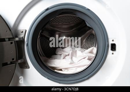 Gros plan d'un tambour de lave-linge à chargement frontal rempli de linge blanc, illustrant l'entretien du linge, la conception de l'appareil et les tâches ménagères Banque D'Images