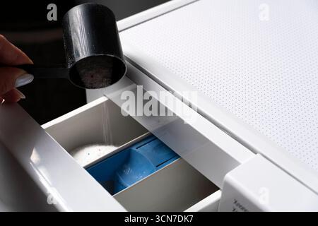 Gros plan de la poudre de détergent à lessive blanche versée dans un tiroir de machine à laver. Utile pour les sujets relatifs au nettoyage, aux tâches ménagères ou au nettoyage Banque D'Images