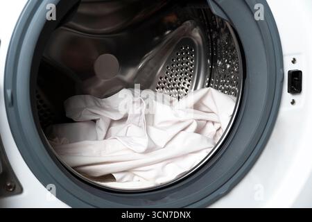Gros plan d'un tambour de lave-linge à chargement frontal rempli de linge blanc, illustrant l'entretien du linge, la conception de l'appareil et les tâches ménagères Banque D'Images