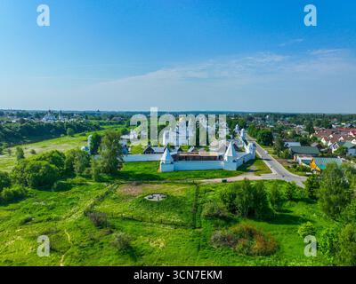 Une vue aérienne large du monastère Pokrovsky avec ses murs blancs et ses bâtiments, avec la ville de Souzdal et ses champs verts en arrière-plan. Banque D'Images