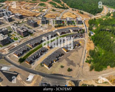 Vue aérienne rapprochée d'un quartier résidentiel moderne à Souzdal, montrant des rangées de maisons de ville nouvellement construites et d'immeubles d'habitation en construction. Banque D'Images