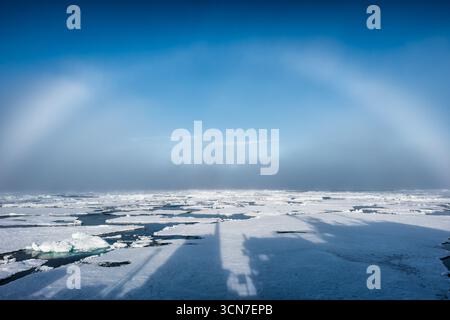 Sjuoyane sept îles Svalbard Océan Arctique Norvège // SVALBARD ET Jan MAYEN — Une vaste étendue de glace de mer flotte dans l'Océan Arctique au large des côtes de Svalbard, en Norvège. Les floes de glace sont entrecoupées d'eau sombre, créant un contraste frappant avec la glace blanche brillante et le ciel bleu clair. La scène capture la beauté lointaine et accidentée de l'environnement arctique. L'ombre d'un navire ou d'une structure est visible sur la glace au premier plan, suggérant la présence humaine dans cette région éloignée. Le Svalbard est un archipel situé dans l'océan Arctique, à mi-chemin entre la Norvège continentale et le pôle Nord Banque D'Images