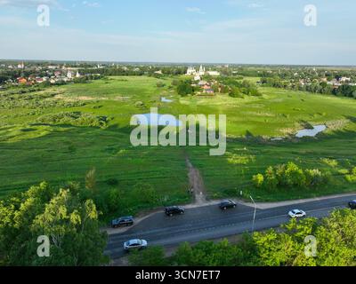 Souzdal, Russie - 12 mai 2024 : Une vue aérienne large d'une vaste prairie verte avec de petits étangs et un chemin de terre, avec la ville de Souzdal et ses monastères Banque D'Images