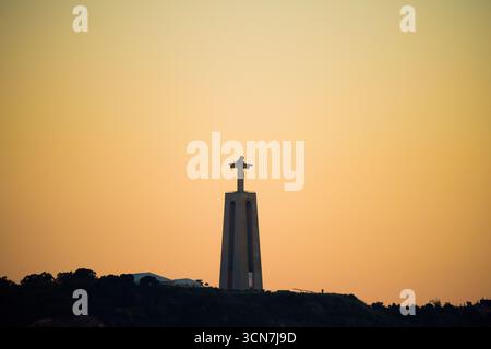 Sanctuaire du Christ Roi Almada Portugal / ALMADA, Portugal — le Sanctuaire du Christ Roi se dresse majestueusement sur une falaise surplombant Lisbonne de l'autre côté du Tage. Inspiré par la statue du Christ Rédempteur de Rio de Janeiro, ce monument présente une grande figure de Jésus avec les bras tendus au sommet d'un grand piédestal. Inauguré en 1959, il offre une vue panoramique à couper le souffle sur Lisbonne et le pont emblématique du 25 avril. Banque D'Images