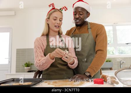 Couple diversifié dans les tabliers rouler la pâte et couper avec emporte-pièce à la cuisine moderne Banque D'Images