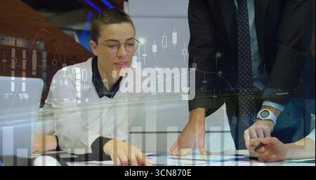 Penchée sur des lunettes - femme européenne examinant des graphiques au bureau avec un ordinateur portable, un stylo et des superpositions graphiques Banque D'Images