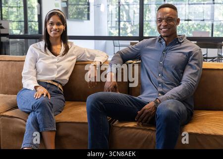 Divers collègues souriants, portant des montres-bracelets sur un canapé en cuir marron dans le salon de bureau Banque D'Images