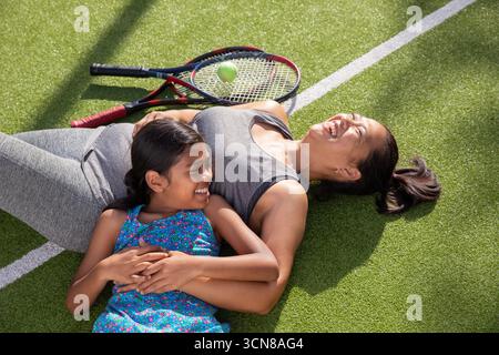Mère asiatique et fille allongée sur un court de tennis en gazon vert sous la lumière du soleil avec des raquettes, balle Banque D'Images