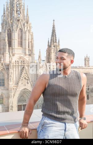 Un homme portant une chemise rayée noire et blanche se tient sur un balcon donnant sur une ville. Il sourit et il profite de la vue Banque D'Images