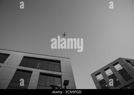 Avion volant au-dessus des immeubles de bureaux modernes en noir et blanc Banque D'Images