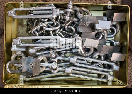 Une boîte d'objets métalliques assortis, y compris des chaînes et des boulons. L'étain est ouvert et les objets sont dispersés autour Banque D'Images