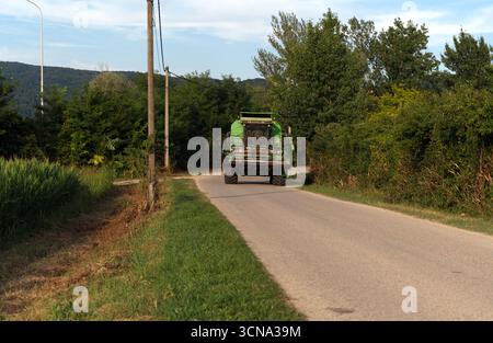 Une grande moissonneuse-batteuse verte emprunte une route de campagne étroite et sinueuse, laissant un petit sillage de poussière sur son passage. Banque D'Images