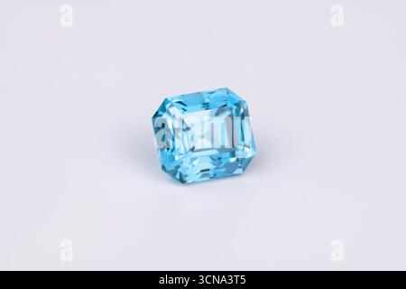 Une pierre précieuse bleue repose sur une surface blanche. La pierre est taillée en une forme rectangulaire et il est un saphir bleu Banque D'Images