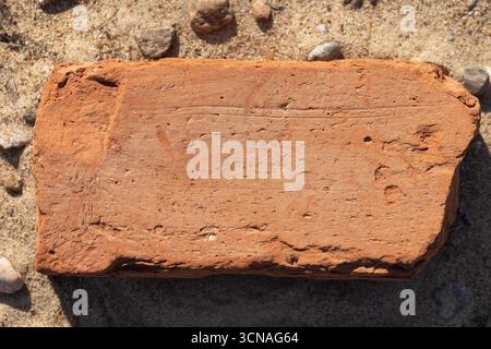Une brique solitaire reposant sur un sol sablonneux, soulignant sa texture et sa couleur terreuse. Un concept de construction, de simplicité et de matériaux naturels Banque D'Images