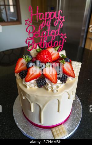 Un gâteau d'anniversaire tardif bien présenté avec une sélection de fruits mélangés décorant le dessus et un glaçage au chocolat blanc Banque D'Images