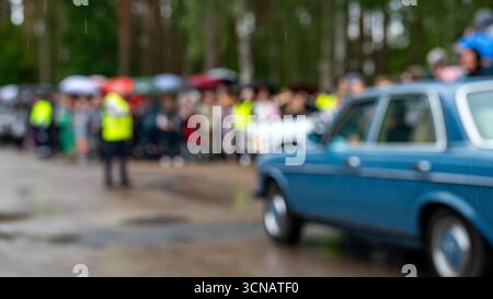 Les gens se rassemblent sous des parapluies alors que les voitures s'alignent pour un événement dans une zone boisée un jour de pluie Banque D'Images