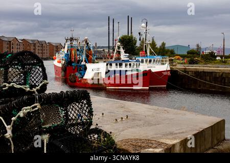 Deux bateaux de pêche rouge et blanc éclatants amarrés dans un port, avec des casiers à homard au premier plan. Banque D'Images
