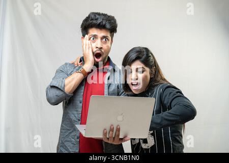 Un jeune couple avec une expression choquée, regardant un ordinateur portable. Banque D'Images