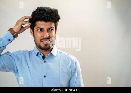 Un jeune homme se grattant la tête avec une expression confuse et incertaine. Banque D'Images