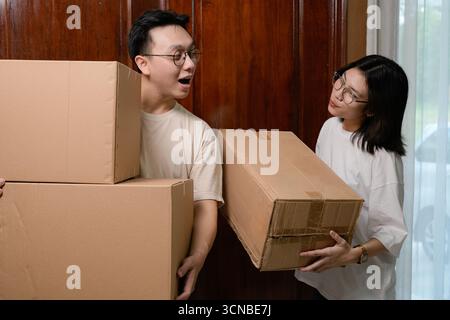 Couples déplaçant des boîtes dans le couloir de la maison, partageant des sourires tout en transportant des paquets de carton Banque D'Images
