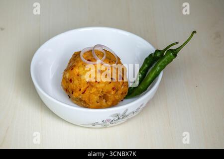 Délicieux Aloo Bharta sur un bol blanc avec des piments verts et des rondelles d'oignon sur fond de bois. C'est la nourriture traditionnelle bengali (Bangladesh). Banque D'Images