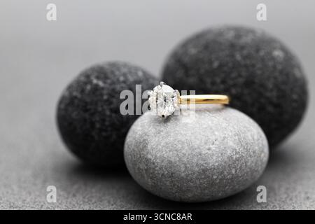 Une bague en diamant est sertie dans une bande d'or et repose sur une pile de roches grises. L'anneau est le point focal de l'image, et les roches servent de contr Banque D'Images