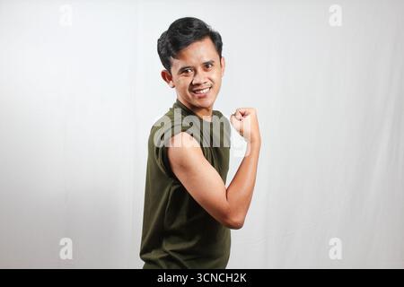 Jeune homme confiant fléchissant les biceps avec le sourire, mettant en valeur la forme physique et la santé pour le contenu de style de vie Banque D'Images