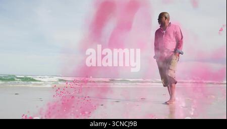 Homme marchant portant une chemise rose et un short le long du rivage, avec de la poudre rose et des vagues, espace de copie Banque D'Images
