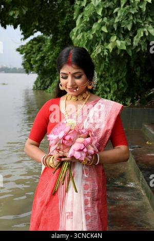 Portrait de belle jeune femme indienne, vêtue d'un saree traditionnel, avec des bijoux en or, tenant délicatement des fleurs dans ses mains devant le Banque D'Images