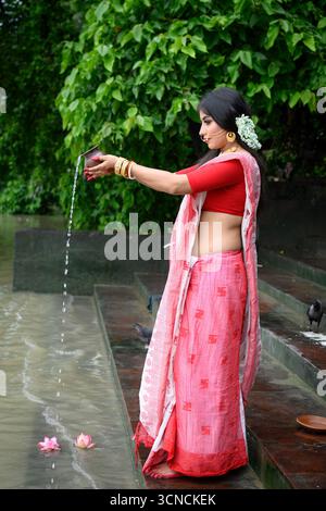 Portrait de belle jeune femme indienne, vêtue de saree traditionnel avec des bijoux en or, versant de l'eau sacrée dans le fleuve Gange pendant WO quotidien Banque D'Images