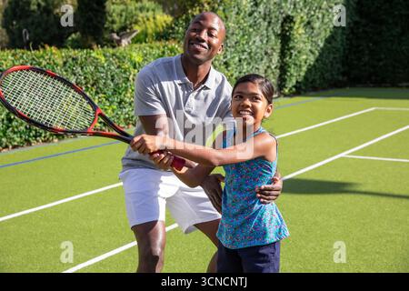 Père et fille divers pratiquant le swing de tennis sur un court de tennis avec raquette rouge et noire Banque D'Images