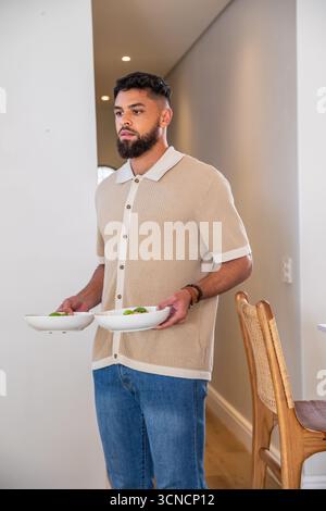 Homme tenant deux saladiers blancs et debout dans la salle à manger moderne près de la chaise Banque D'Images