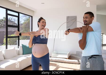 Diverses amies féminines étirant les bras sur la poitrine dans un salon lumineux avec des trackers de fitness Banque D'Images