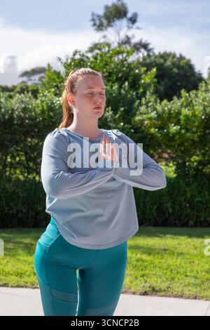 Femme adulte portant un haut athlétique gris et des leggings sarcelle pratiquant la prière de yoga pose sur le parc Banque D'Images