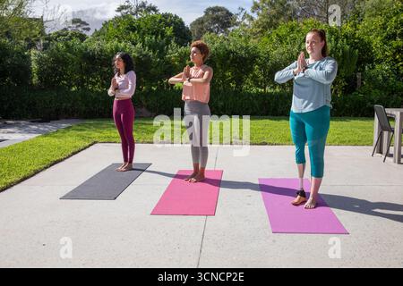 Diverses amies féminines portant des vêtements de sport pratiquant le yoga sur patio avec des tapis, des trackers de fitness Banque D'Images