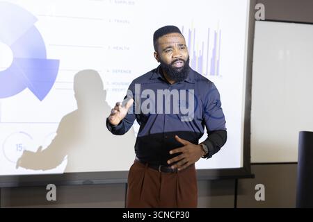 Homme afro-américain présentant un diagramme circulaire et un graphique à barres sur l'écran de projection dans la salle de conférence Banque D'Images