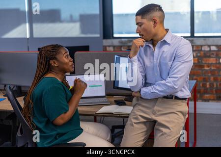 Divers collègues discutent des graphiques de données sur ordinateur portable au bureau avec moniteurs, ordinateur portable, smartphone Banque D'Images